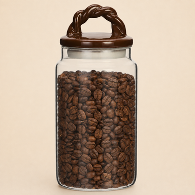 Glass storage jar filled with coffee beans, featuring a brown ceramic braided-handle lid against a warm beige background.