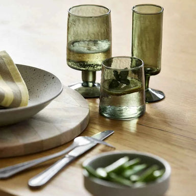 et of two dark green hand-blown drinking glasses styled on an elegant dining table.