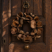 Natural brown dried botanical wreath featuring sculptural seed pods in warm walnut and chocolate tones, hanging on an antique dark wooden exterior door.