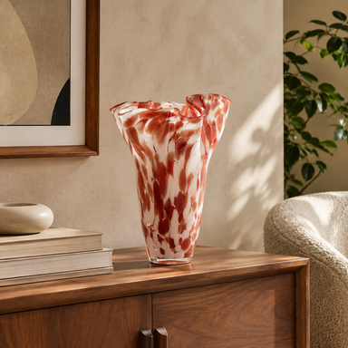 Pink and red sculptural wavy glass vase displayed on a walnut sideboard in a mid-century modern living room.