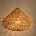Nest-inspired sculptural pendant light crafted from intricately woven natural paper and metal, featuring an organic rounded silhouette and warm glowing bulb against a dark beige background.