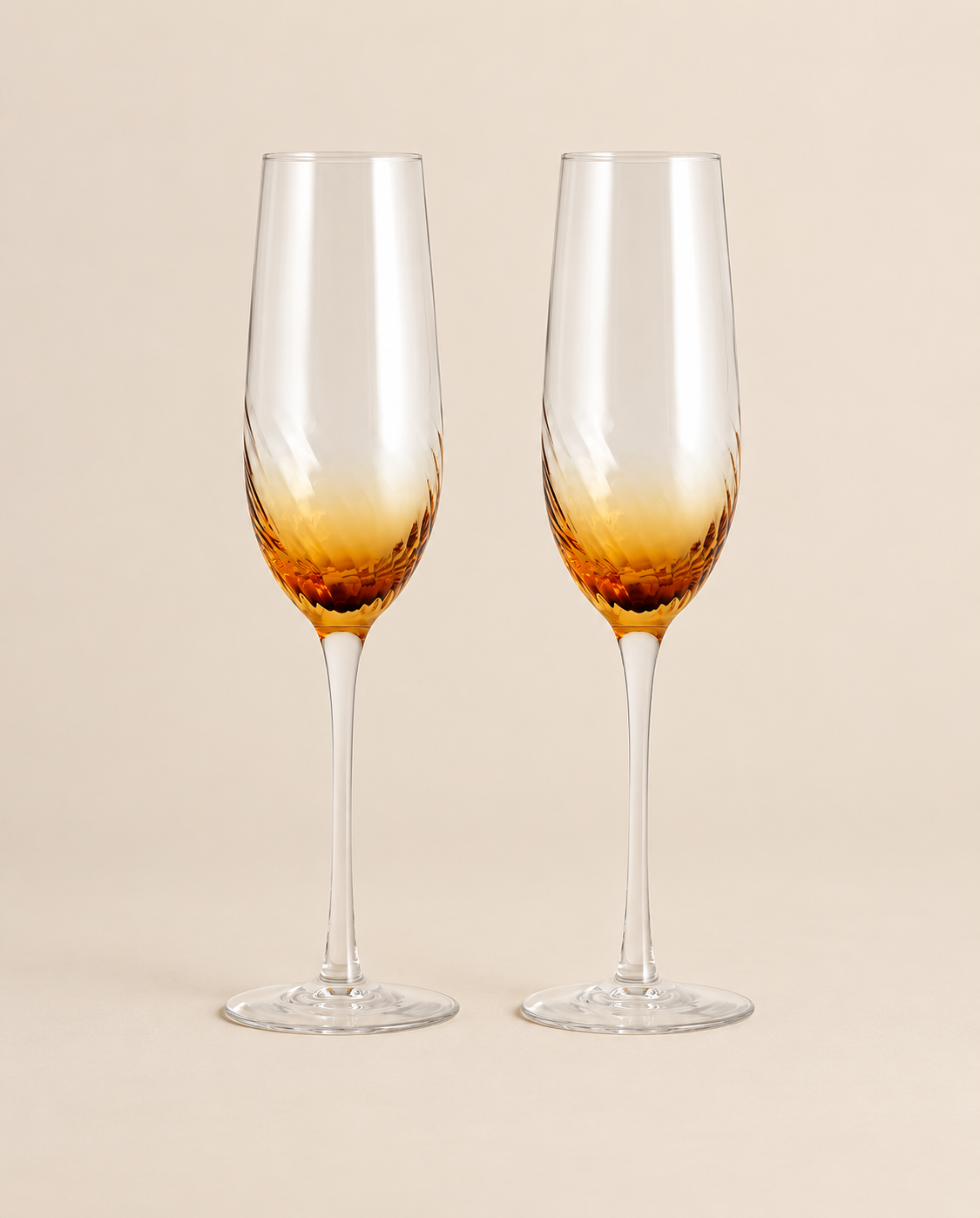 Two champagne flutes with amber textured bowls and clear slender stems on a light beige background.