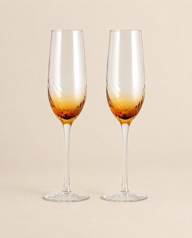 Two champagne flutes with amber textured bowls and clear slender stems on a light beige background.