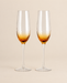 Two champagne flutes with amber textured bowls and clear slender stems on a light beige background.