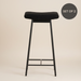 Black metal bar stool with soft teddy upholstery, a padded seat and a contemporary design.