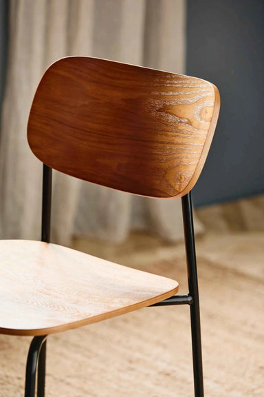 Close-up of the walnut plywood grain and smooth finish on the mid-century dining chair with black metal legs.