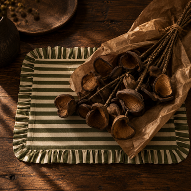 Sculptural antique-brown botanical seed pod stems arranged on a dark walnut table with olive striped fabric.