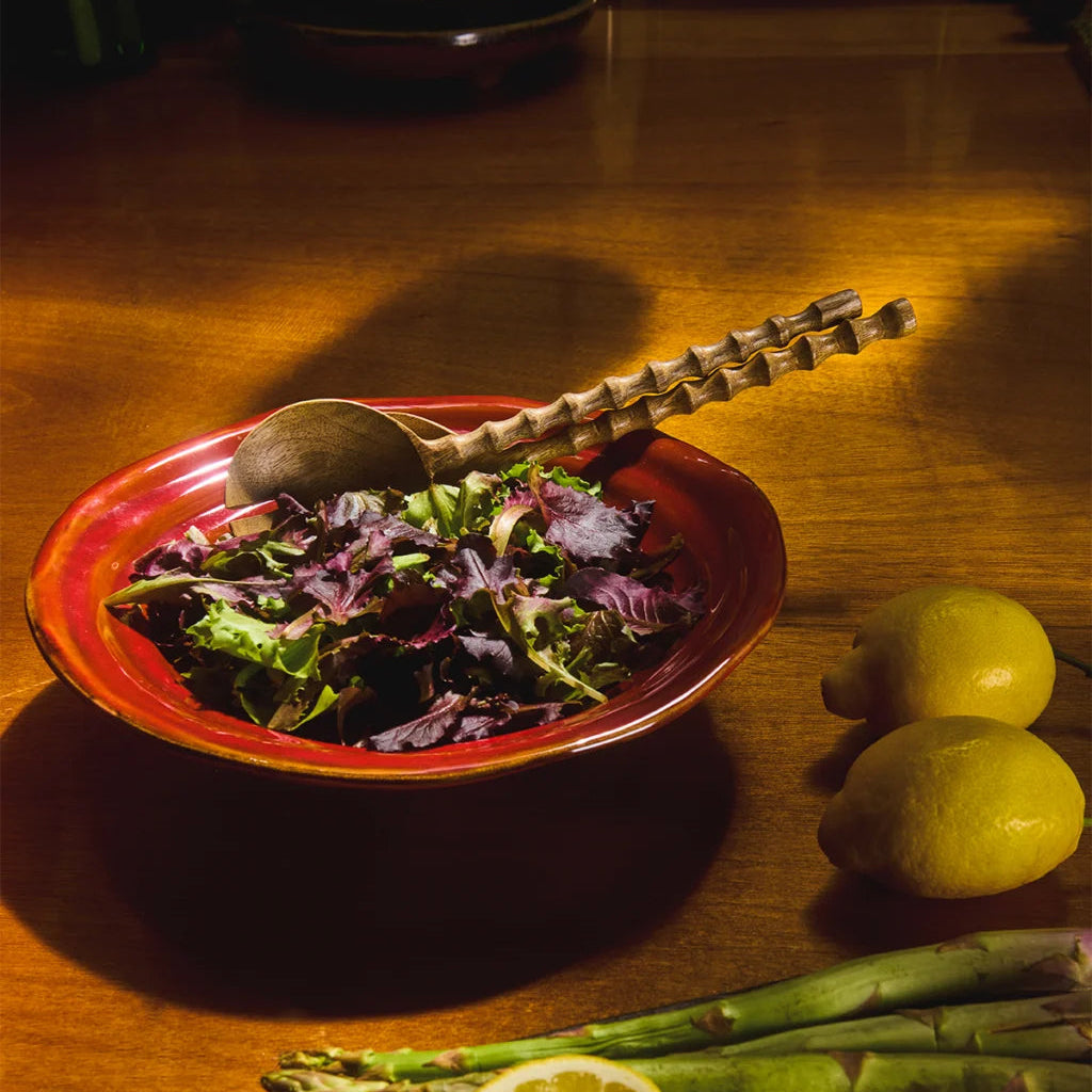 Glossy red ceramic salad bowl with a softly curved shape and irregular rim, photographed against a neutral background