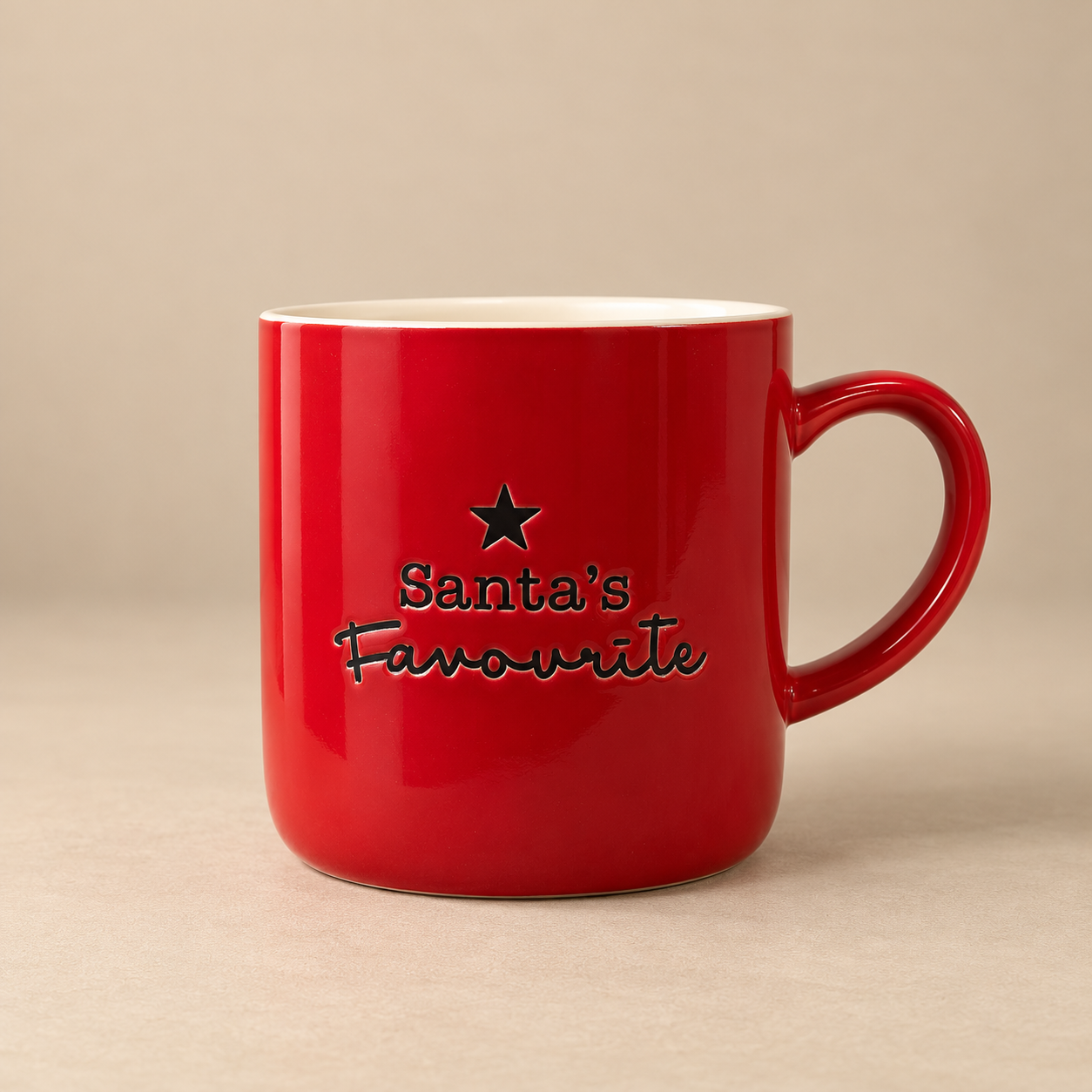 Glossy red ceramic Christmas mug featuring black Santa's Favourite lettering and a decorative star, with a curved red handle and cream interior, photographed against a warm beige background.